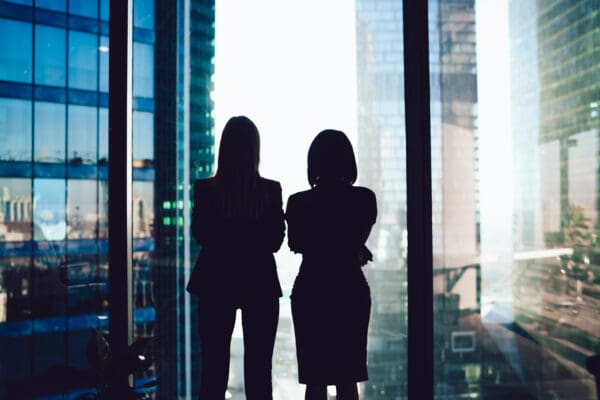 Back view of female colleagues in formal wear standing near window